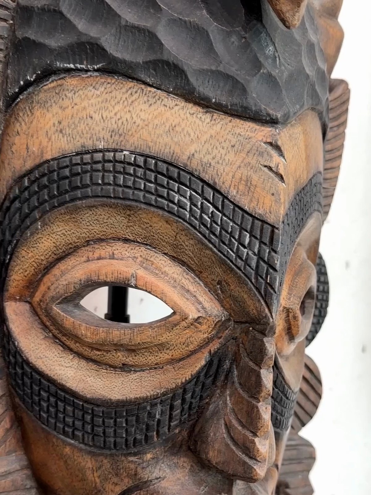 A carved wooden mask on a stand in a white gallery room