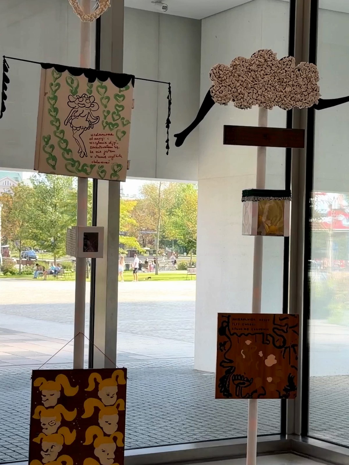 Hanging textile and mixed-media works in front of a tall museum window