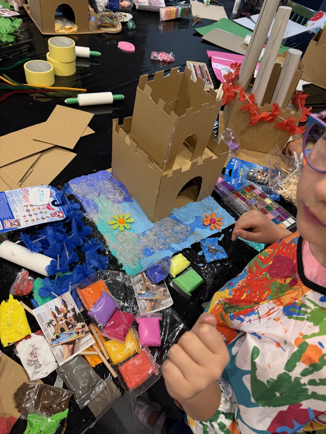 A cardboard castle standing on its painted seabed, with packets of coloured foam clay waiting on the table