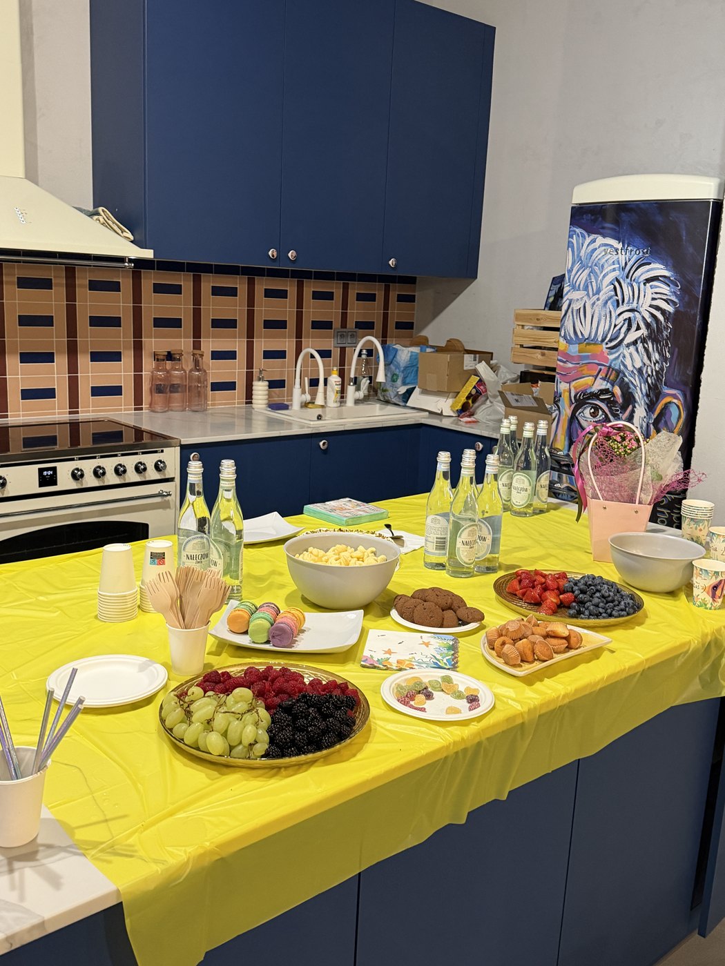 The party table laid out with fruit, macarons and cupcakes on a yellow cloth