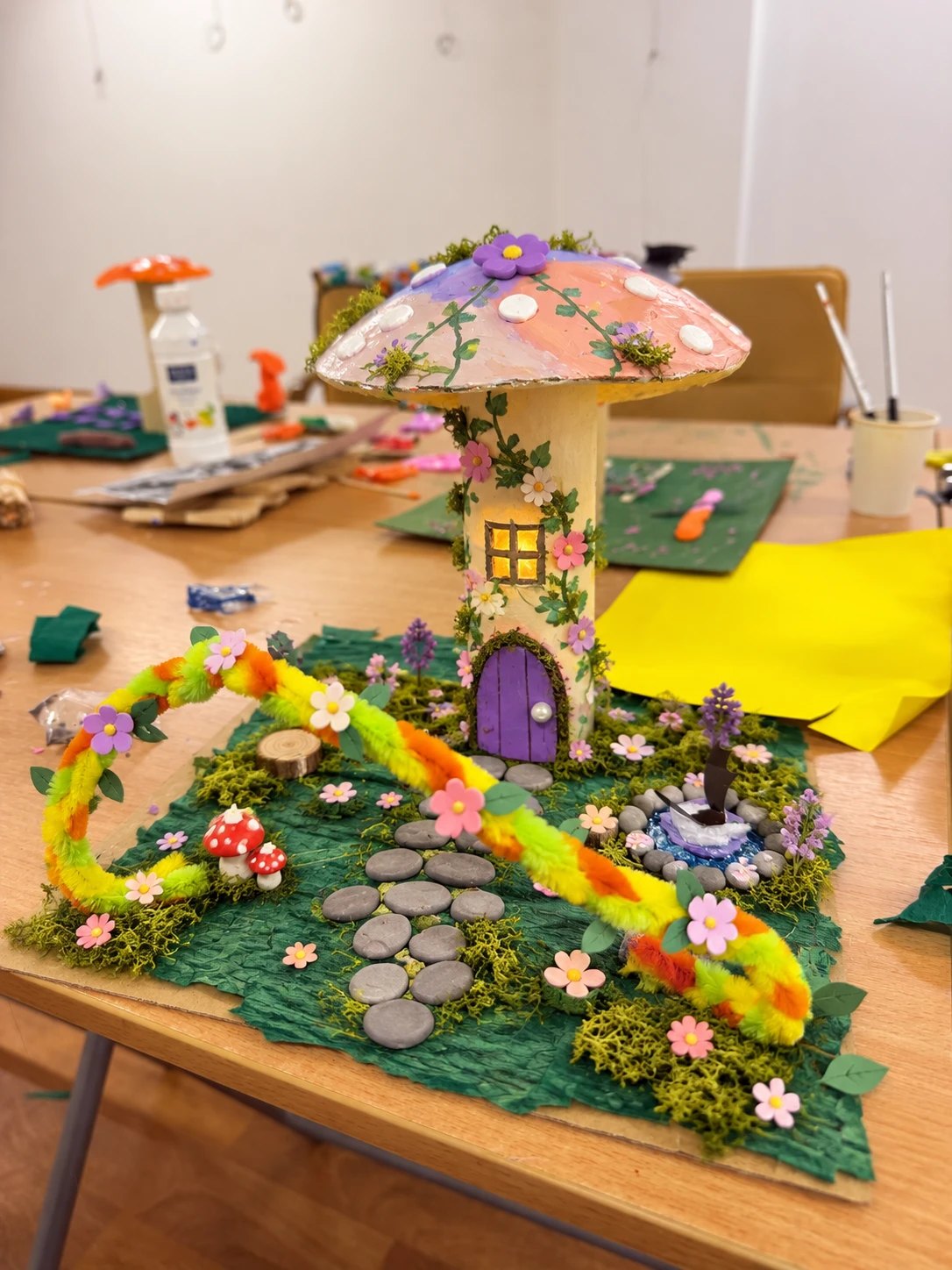 A mushroom fairy house with a glowing window and a little garden, made at the Art for Kids studio