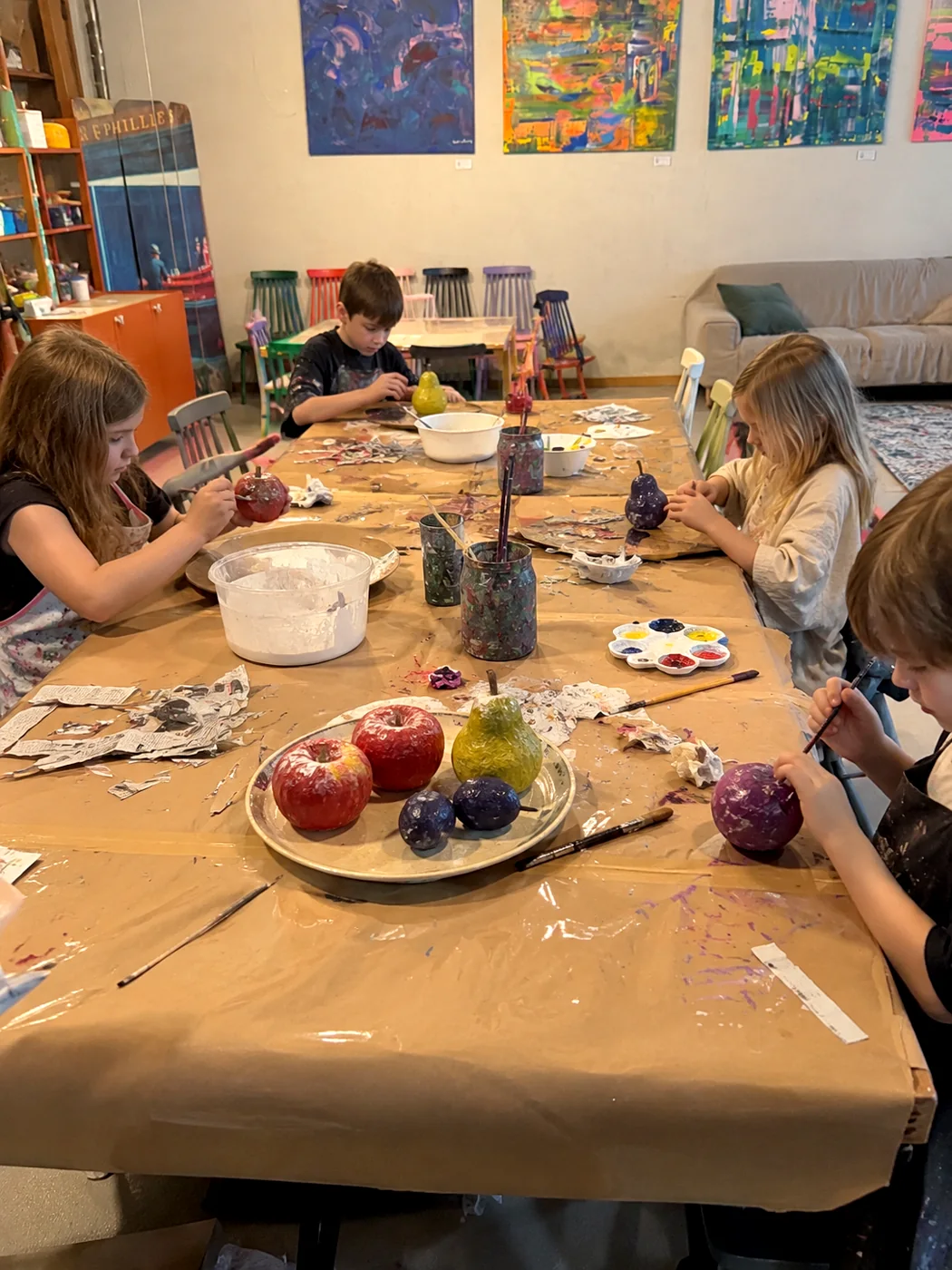 Children painting papier-mâché fruit at the studio: apples, pears and plums in a bowl on the table